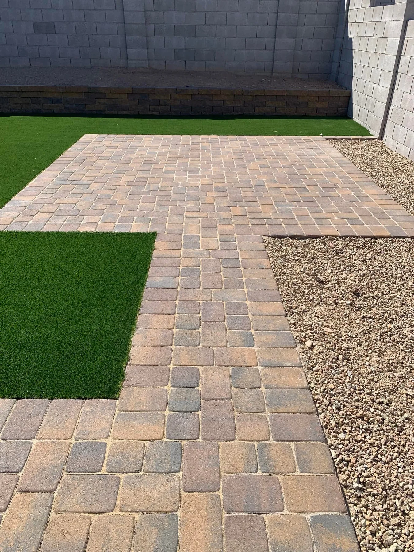 Paver walkway beside artificial turf and decorative rock